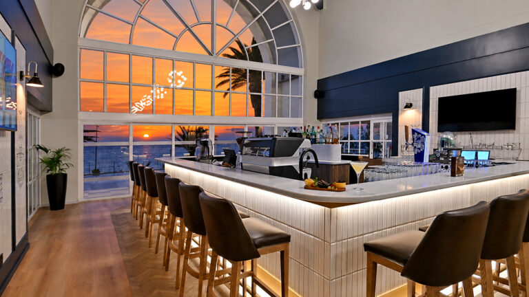 Refurbished bar and restaurant at Courtyard Hotel Gqeberha, featuring modern interiors, illuminated counters and ocean views at sunset.